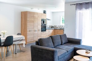 A modern living room with a grey sofa, a dining table with chairs, and a kitchen area with wooden cabinets and a stove. - Gîte Rural Gure Lana: Holiday Home with Mountain View, Wi-Fi, and Air Conditioning (Larressore)