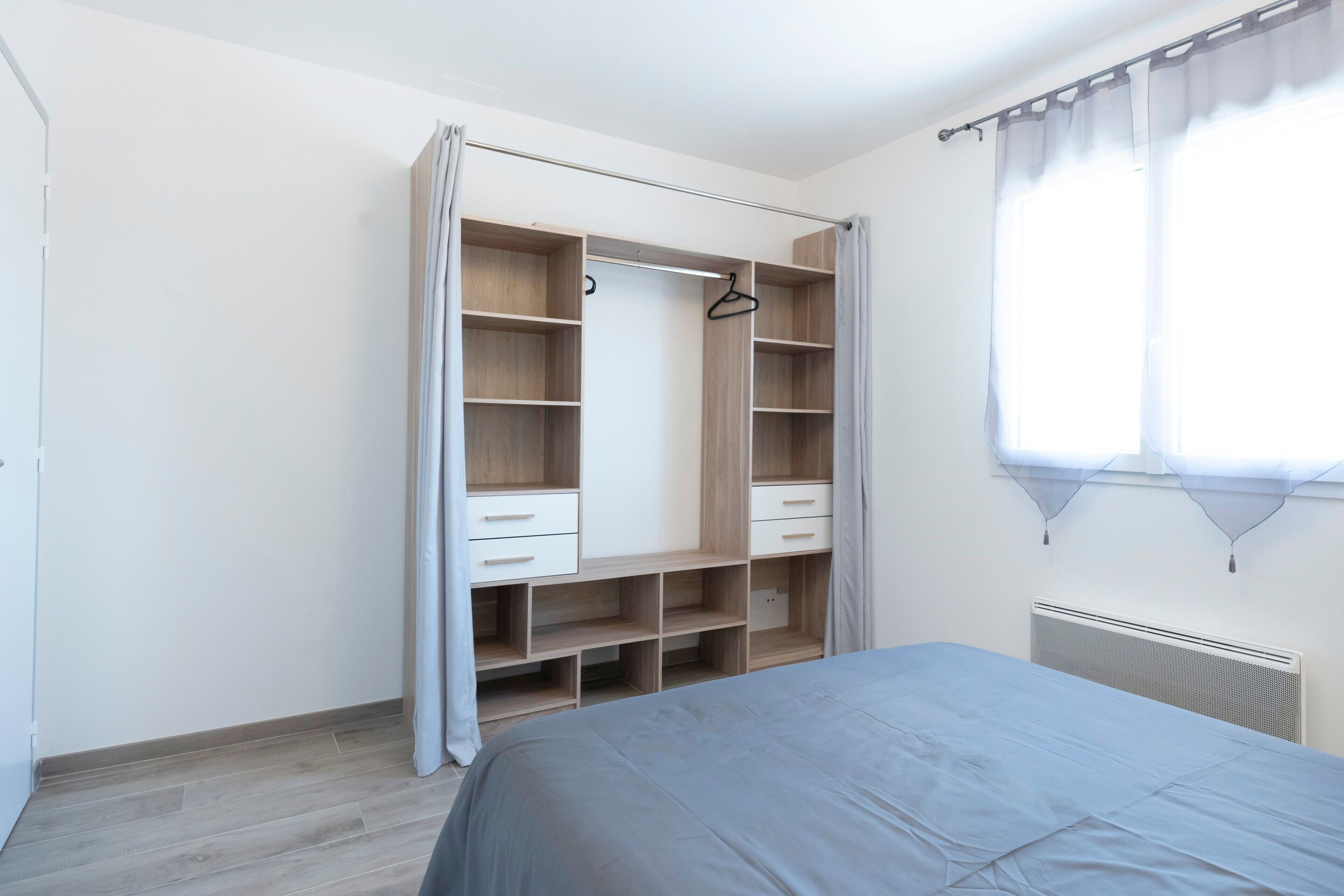 Un dormitorio con cama, un armario con estantes múltiples y un radiador.