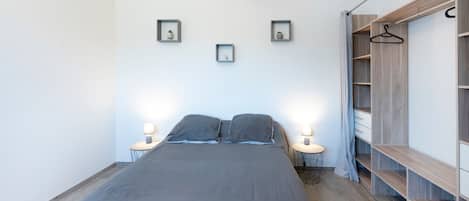 Une chambre à coucher comprenant un lit, des lampes de chevet, une armoire et des étagères fixées au mur.