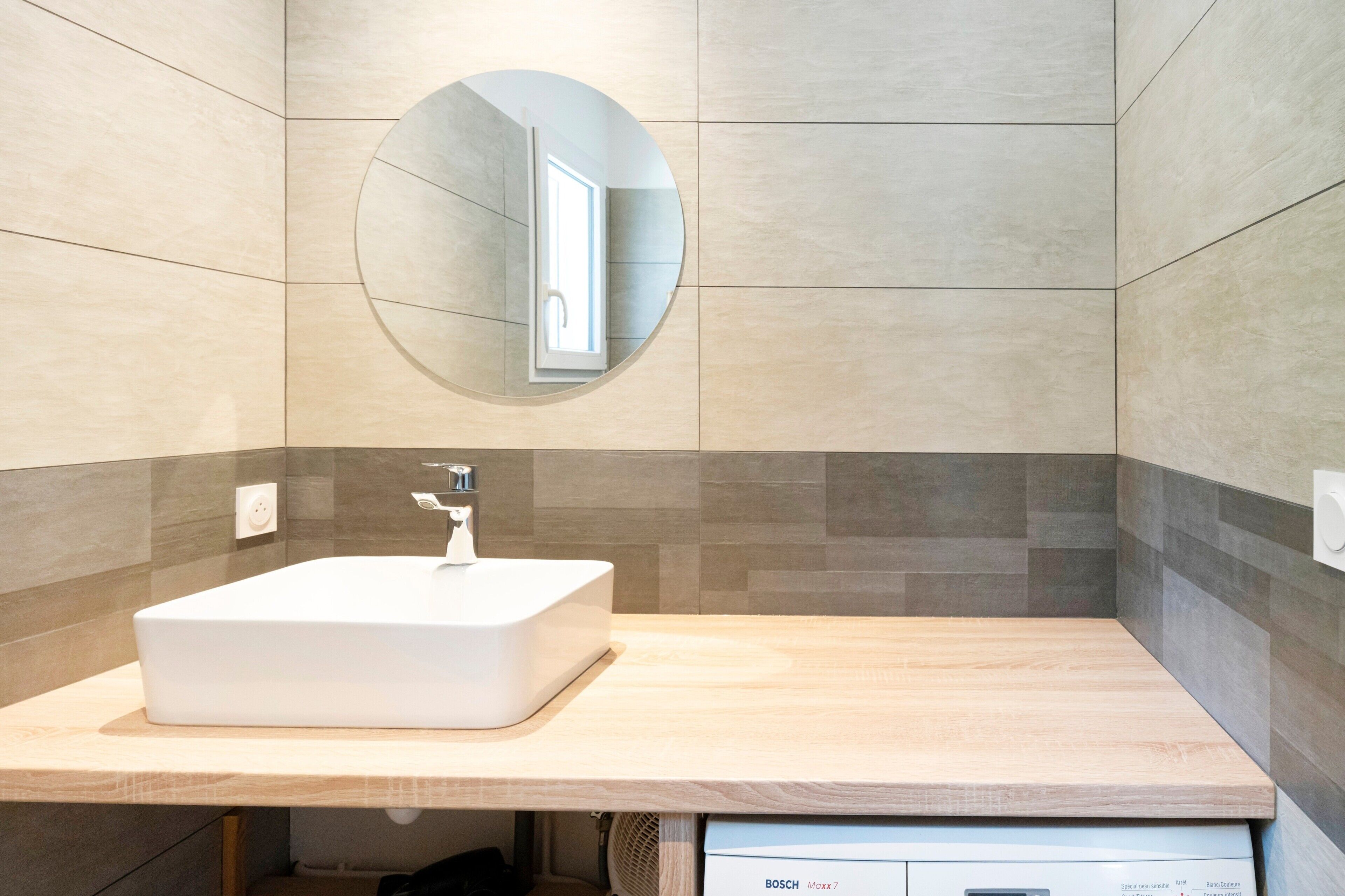 A modern bathroom with a rectangular sink, a round mirror, and a Bosch Maxx 7 water heater.