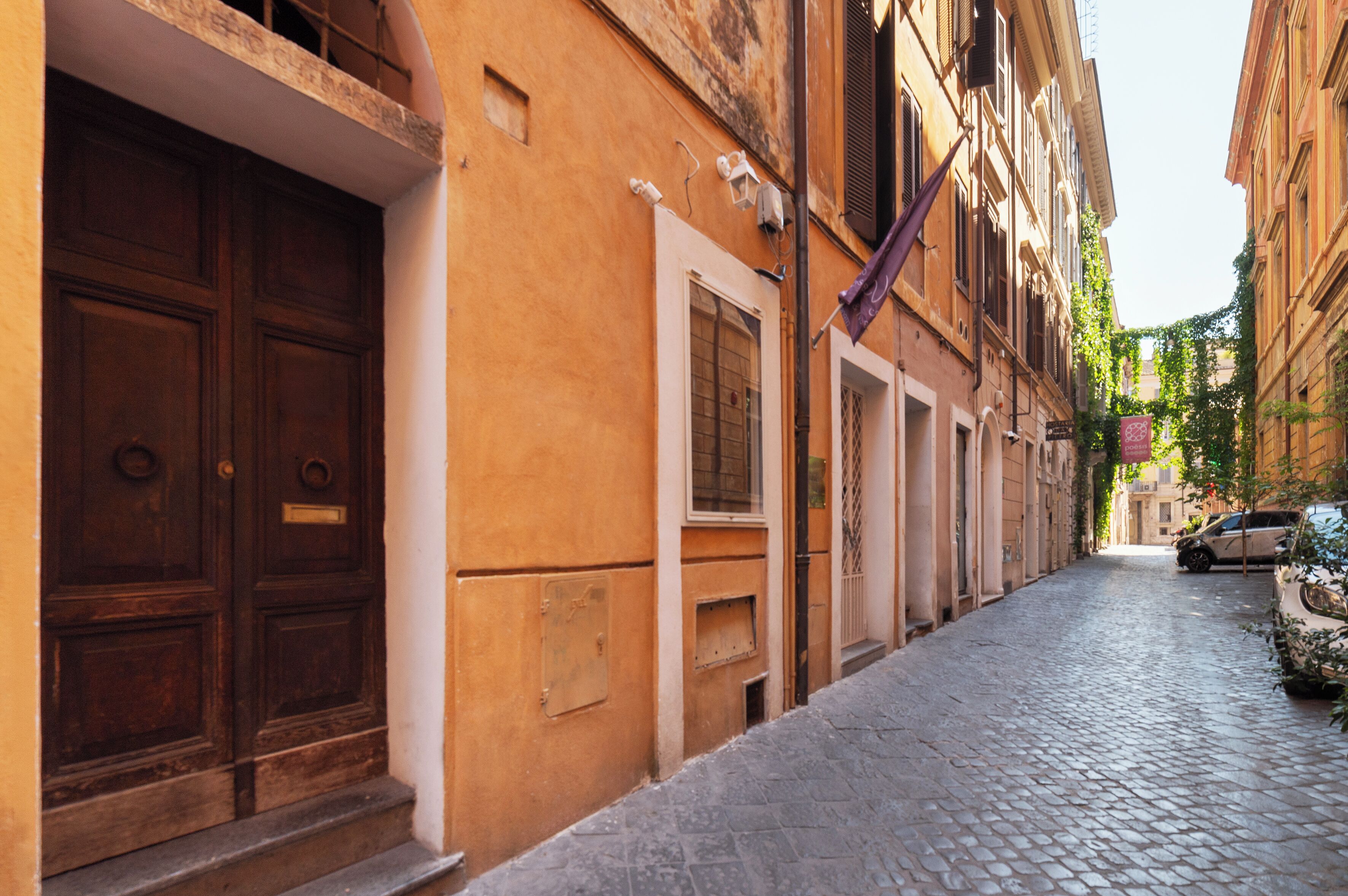 A narrow cobblestone street with traditional buildings, a parked car, and a visible door with a window.