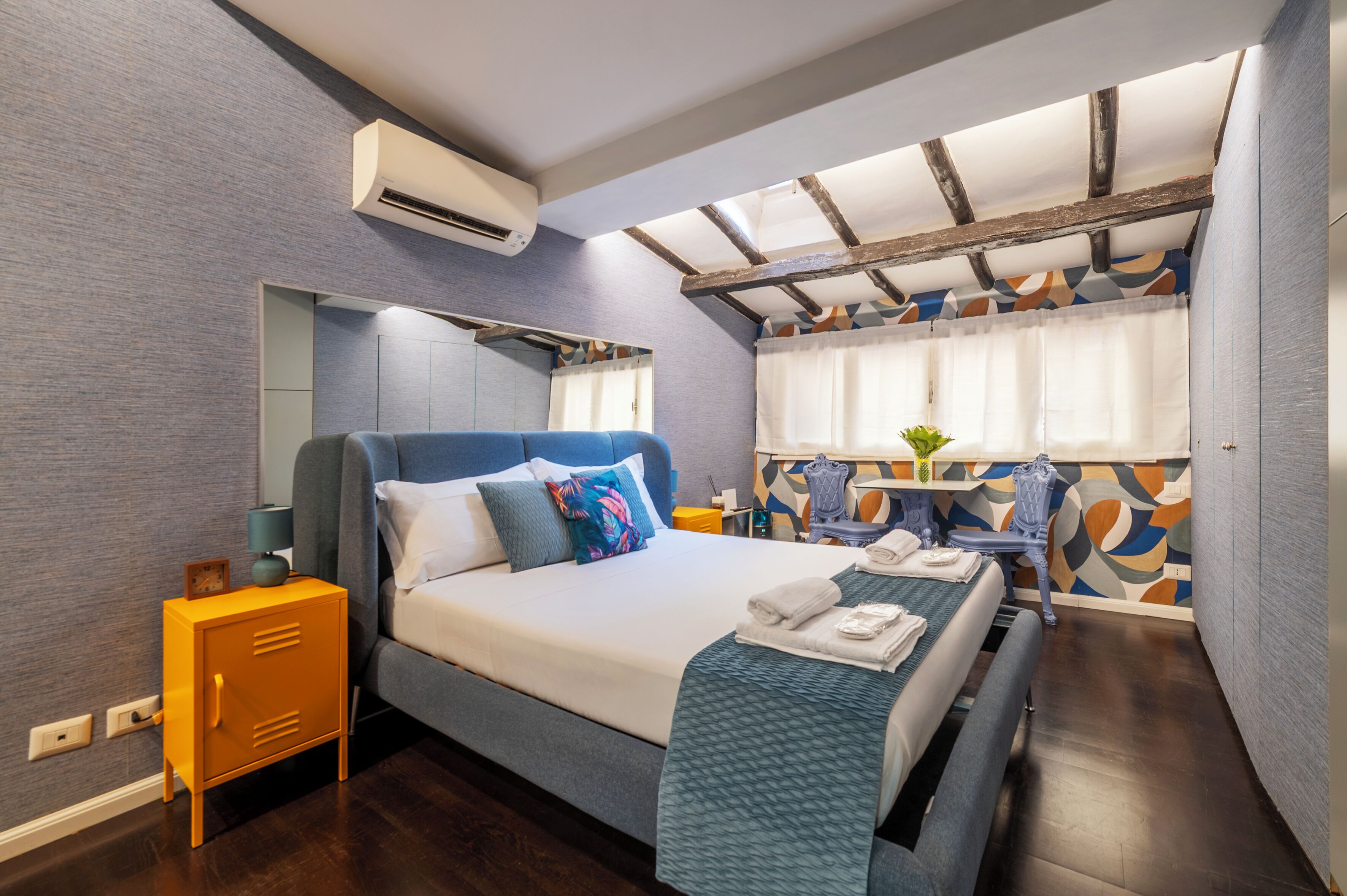 A modern hotel room with a bed, bedside table, air conditioning unit, and a window with curtains.