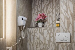 Ein Badezimmer mit Fön, Blumen in einer Vase, einem Schilferdiffusor und einem Thermostat.