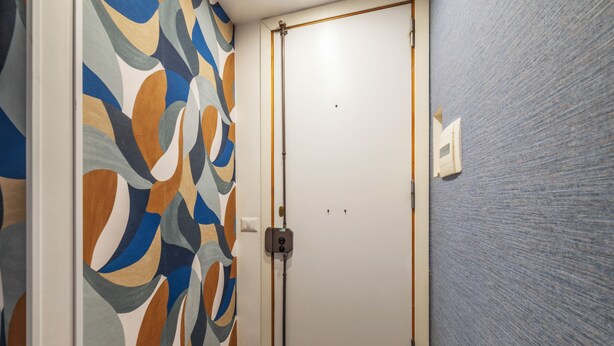 A hallway with a patterned wall, a closed door, and a light switch on the wall. - Via del Corso Quiet Design Studio | Elevator (Roma)