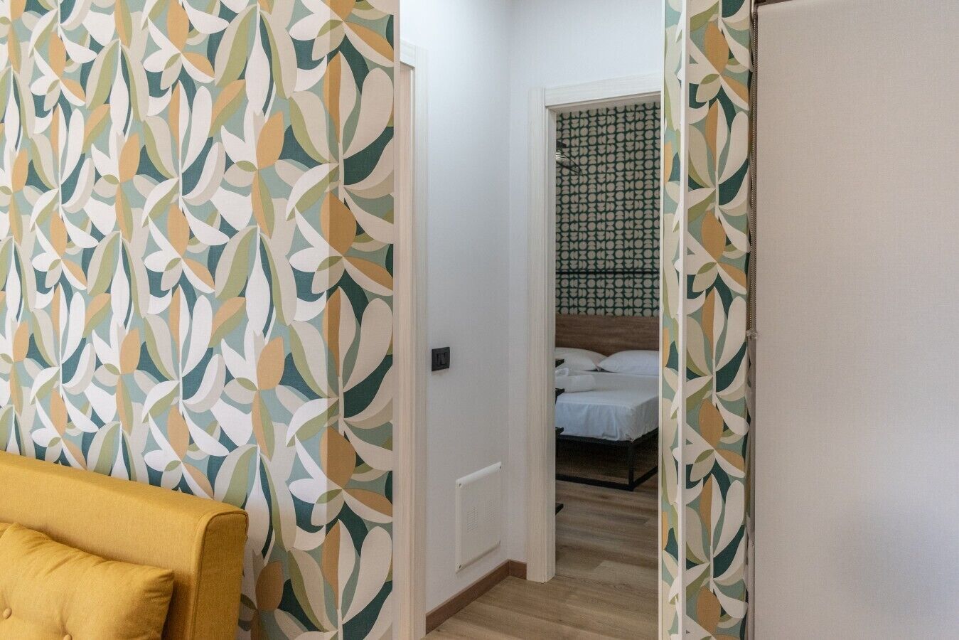 Une pièce avec un papier peint à motifs, un lit recouvert de draps blancs et un fauteuil jaune.