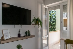 A modern room with a TV, a wooden shelf with decorative items, a potted plant, and an open door leading to an outdoor balcony. - Allegra House - Two-room apartment (Alba Adriatica)