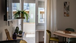 Una habitación moderna con comedor, televisor montado en la pared y balcón con vistas a otros edificios.