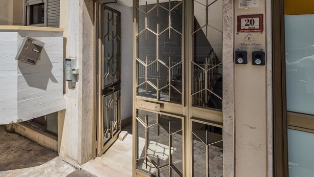 Entrada de un hotel con una verja metálica, un buzón y un cartel que indica la habitación número 20.