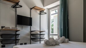 Habitación de hotel con cama, televisor, estante de madera y ventana con cortinas.