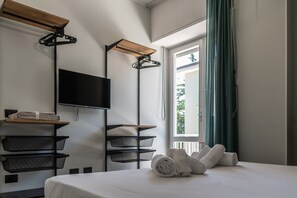 A hotel room with a bed, a TV, a wooden shelf, and a window with curtains. - Allegra House - Two-room apartment (Alba Adriatica)