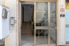 Ein Gebäudeeingang mit einer Treppe, einem Briefkasten und einer Tür mit geometrischem Muster.