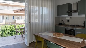 A modern kitchen with a dining area, a balcony with a chair, and a view of a building. - Allegra House - Three-Bedroom Apartment (Alba Adriatica)