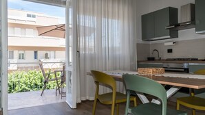 A modern kitchen with a dining area, a balcony with a view of buildings and greenery, and a sliding glass door. - Allegra House - Three-Bedroom Apartment (Alba Adriatica)
