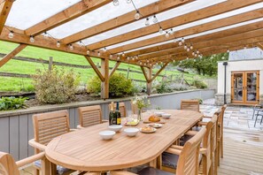An outdoor wooden pergola with string lights, a round wooden table with chairs, and a garden view. - 5 Bed in Garth (oc-c44957) (Treflys)