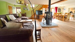 A living room with a sofa, a television, a fireplace, and a dining area with chairs and a table. - 5 Bed in Garth (oc-c44957) (Treflys)