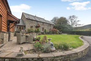 A stone house with a paved patio, outdoor seating, and a well-maintained lawn. - 5 Bed in Garth (oc-c44957) (Treflys)