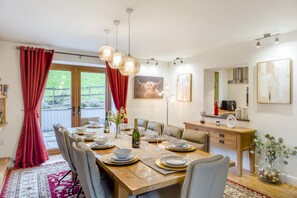 A dining area with a wooden table set for four, a chandelier, and a view of the outdoors. - 5 Bed in Garth (oc-c44957) (Treflys)