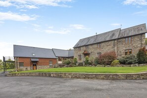 A stone building with a sloped roof, a wooden section, and a well-maintained lawn. - 5 Bed in Garth (oc-c44957) (Treflys)