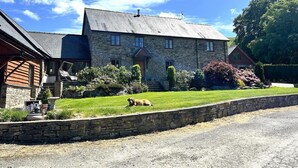 A stone house with a sloped roof, a front porch, and a well-maintained lawn. - 5 Bed in Garth (oc-c44957) (Treflys)
