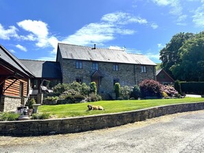 Ein Steinhaus mit einem geneigten Dach, einer Veranda und einem gepflegten Rasen.