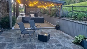 An outdoor patio with a wooden deck, seating area, grill, and string lights. - 5 Bed in Garth (oc-c44957) (Treflys)