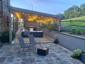 Eine Terrasse im Freien mit Holzdeck, Sitzgruppe, Grill und Lichterketten.