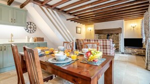 Un coin repas avec une table en bois mise pour le petit-déjeuner, une cuisine avec des meubles bleu clair et une cheminée en pierre.