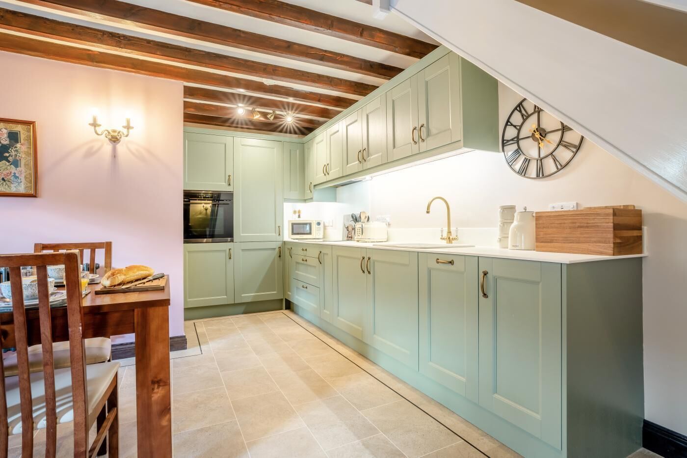Una cucina con mobili verde chiaro, soffitto in legno, un orologio e zona pranzo con tavolo e sedie.