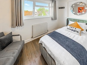 Ein Schlafzimmer mit einem Bett, einem grauen Sofa, einem Fenster mit Vorhängen, einer Heizung und einem Spiegel an der Wand.