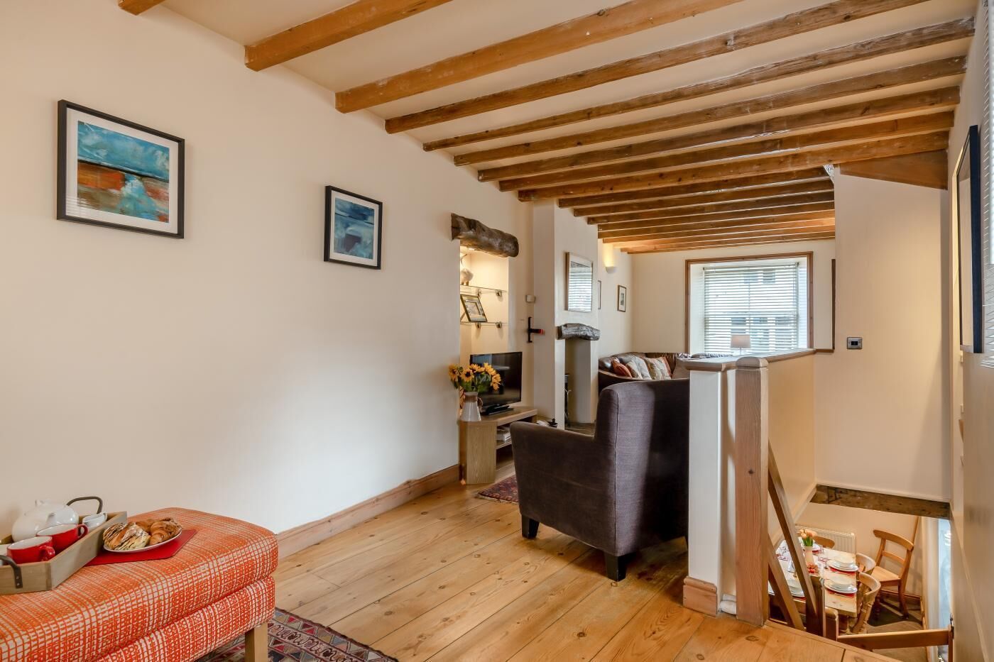 A cozy living room with wooden beams, a sofa, a dining table, and a staircase.