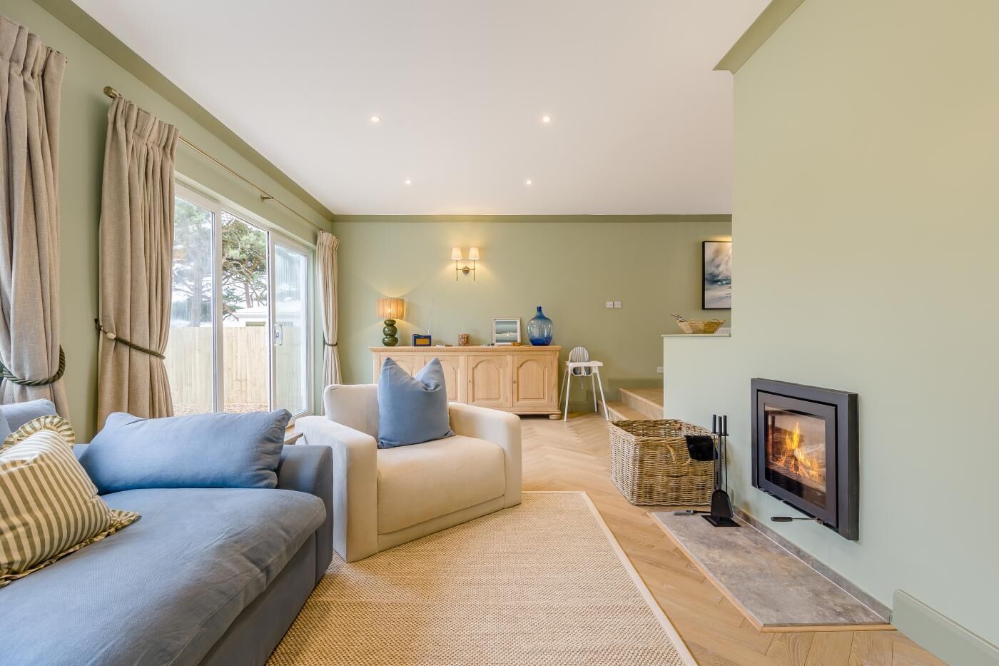 A living room with a sofa, a fireplace, and a kitchen area in the background.