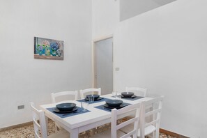 Un'area pranzo con un tavolo e sedie bianche, un quadro appeso al muro e una porta sullo sfondo.