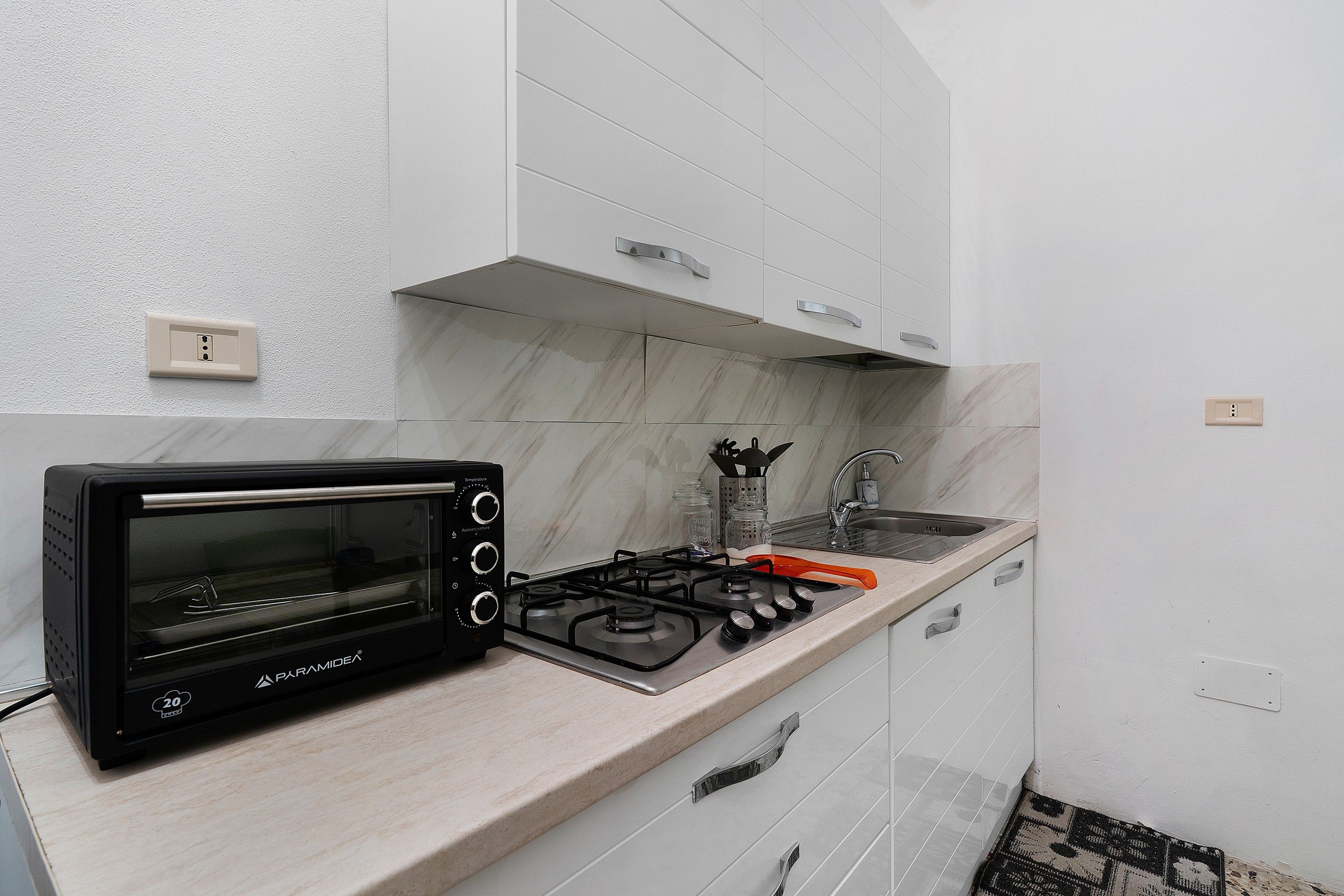 Une cuisine avec un four grille-pain noir, une cuisinière à gaz, un évier et des armoires blanches.