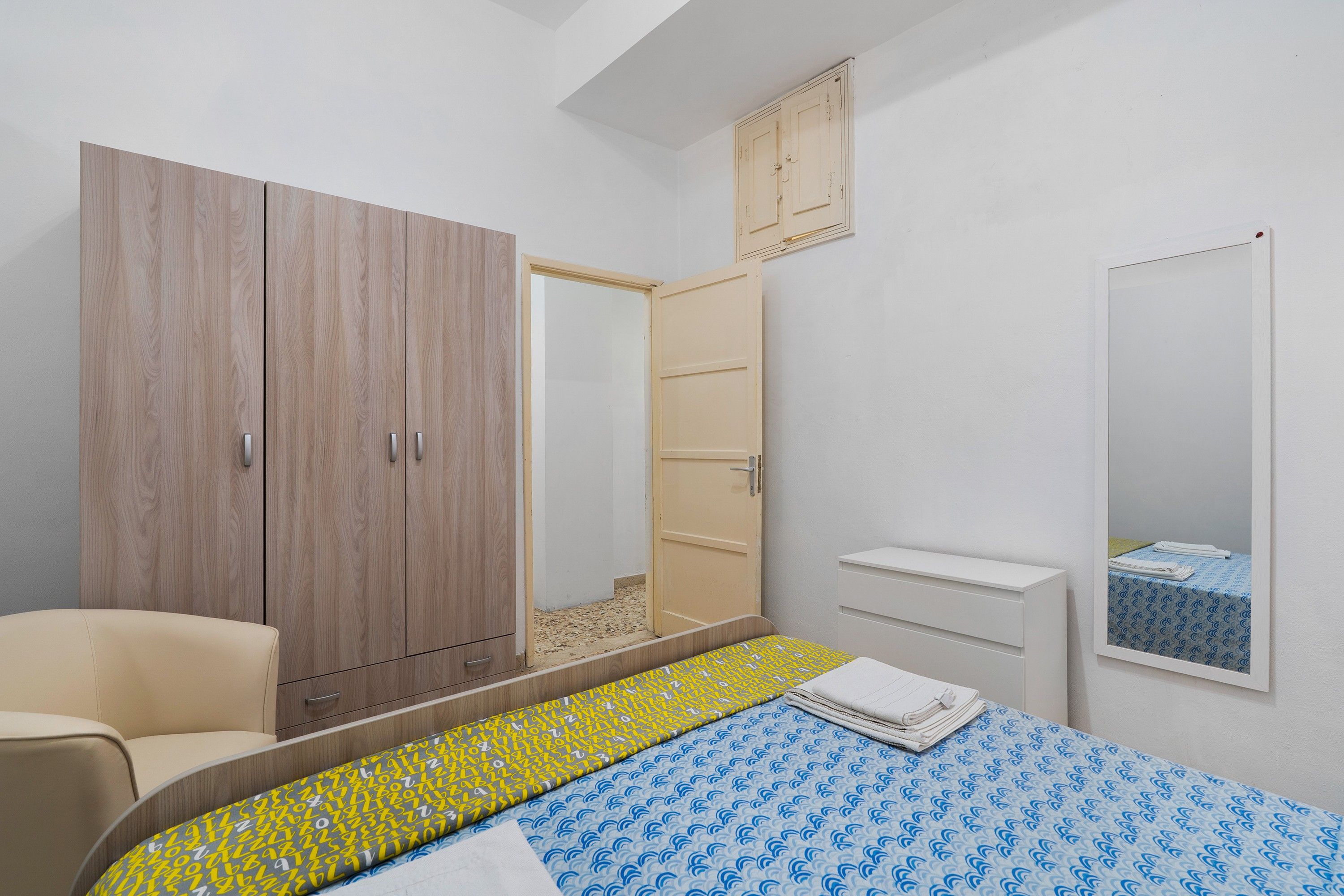 Une chambre à coucher avec un lit, une armoire, un miroir et une petite table de chevet.