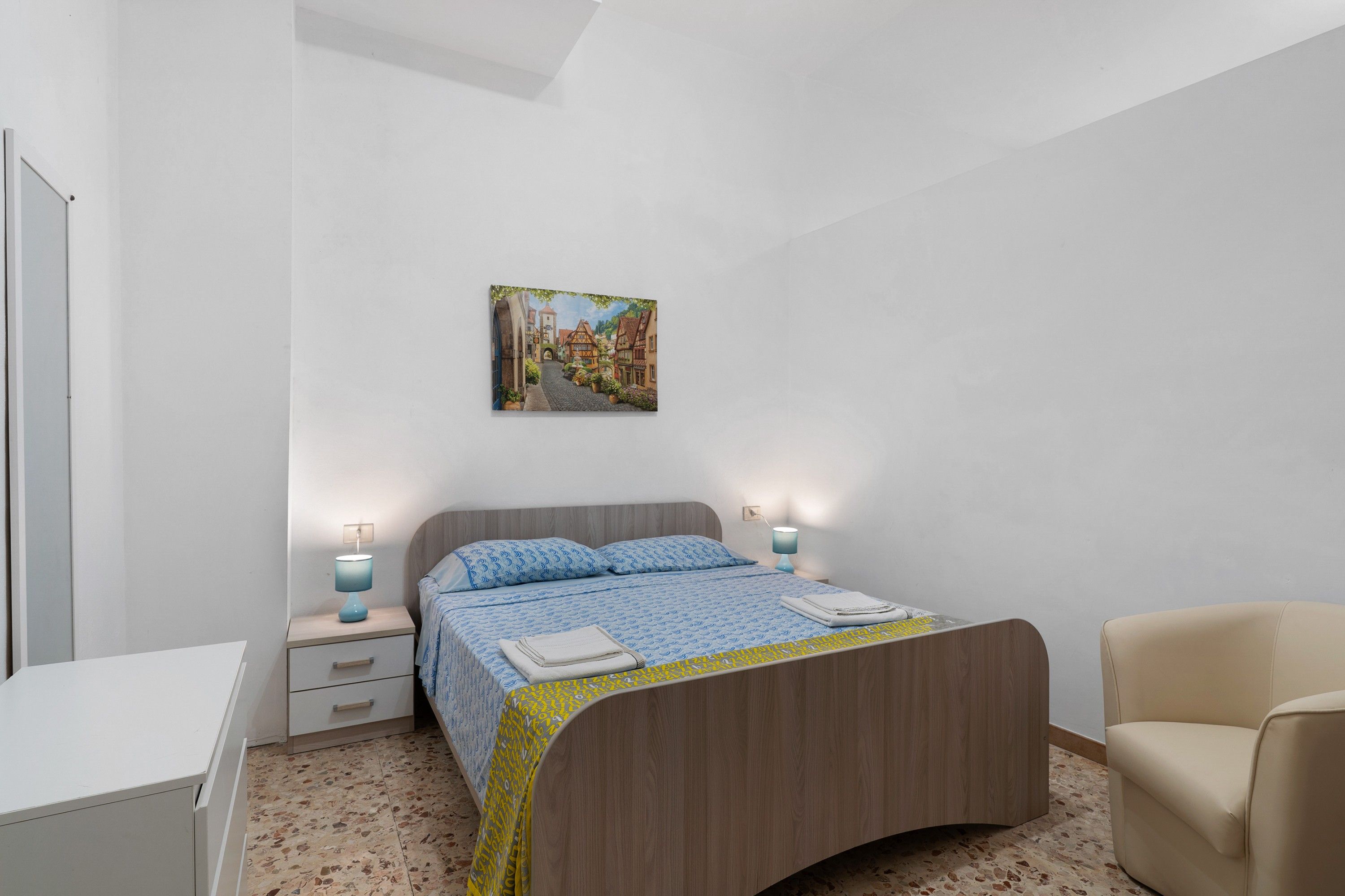 Une chambre à coucher comprenant un lit, des tables de chevet, une chaise, un bureau et un tableau accroché au mur.