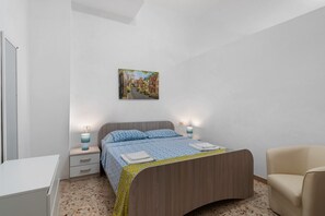 Una camera da letto con un letto, comodini, una sedia, una scrivania e un quadro appeso al muro.