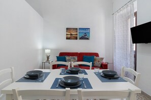 Ein Essbereich mit einem weißen Tisch, gedeckt für vier Personen, einer roten Couch mit gemusterten Kissen und zwei gerahmten Bildern an der Wand.