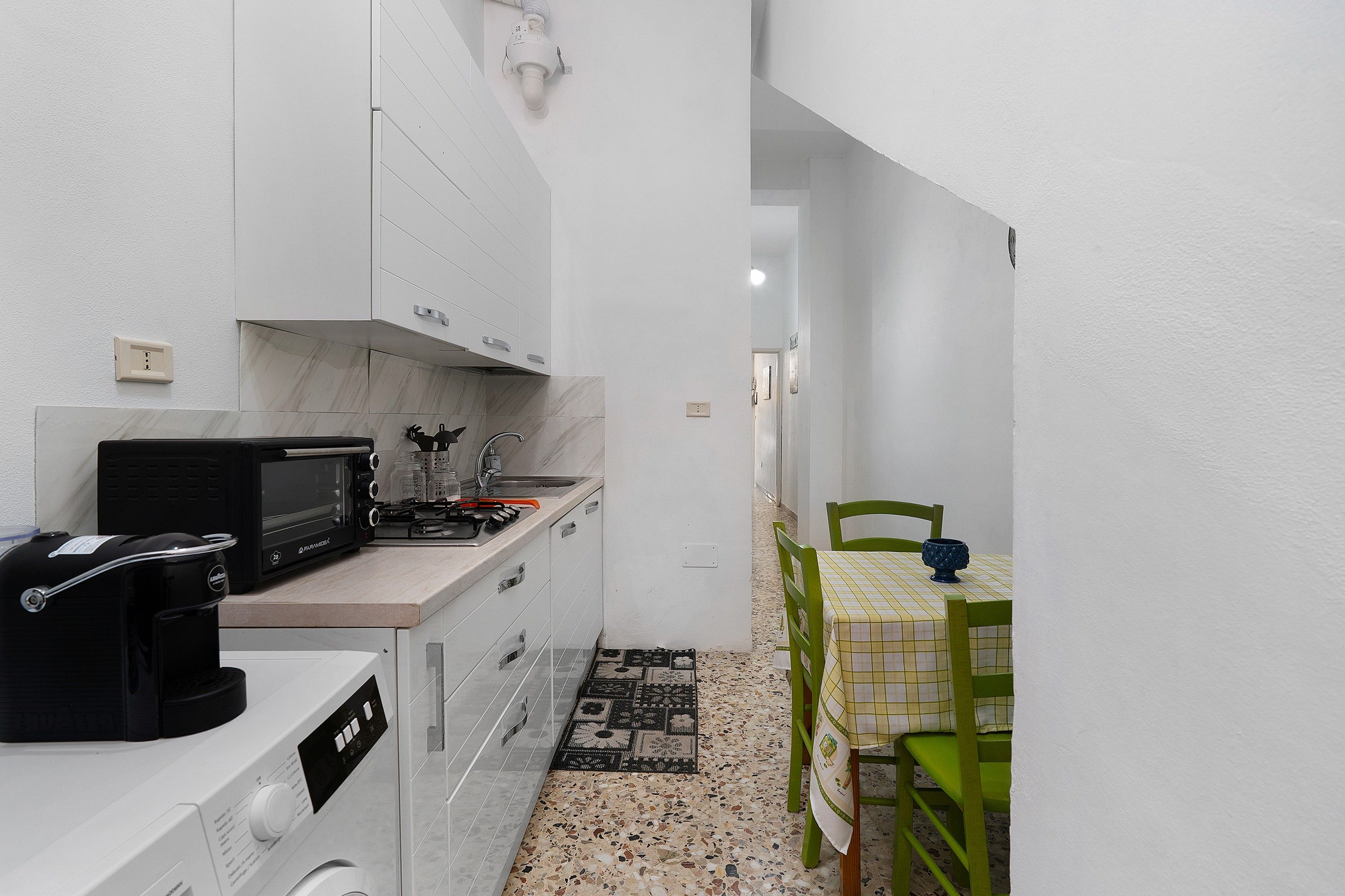 A compact kitchen with white cabinets, a microwave, and a small dining area with a green chair and table.