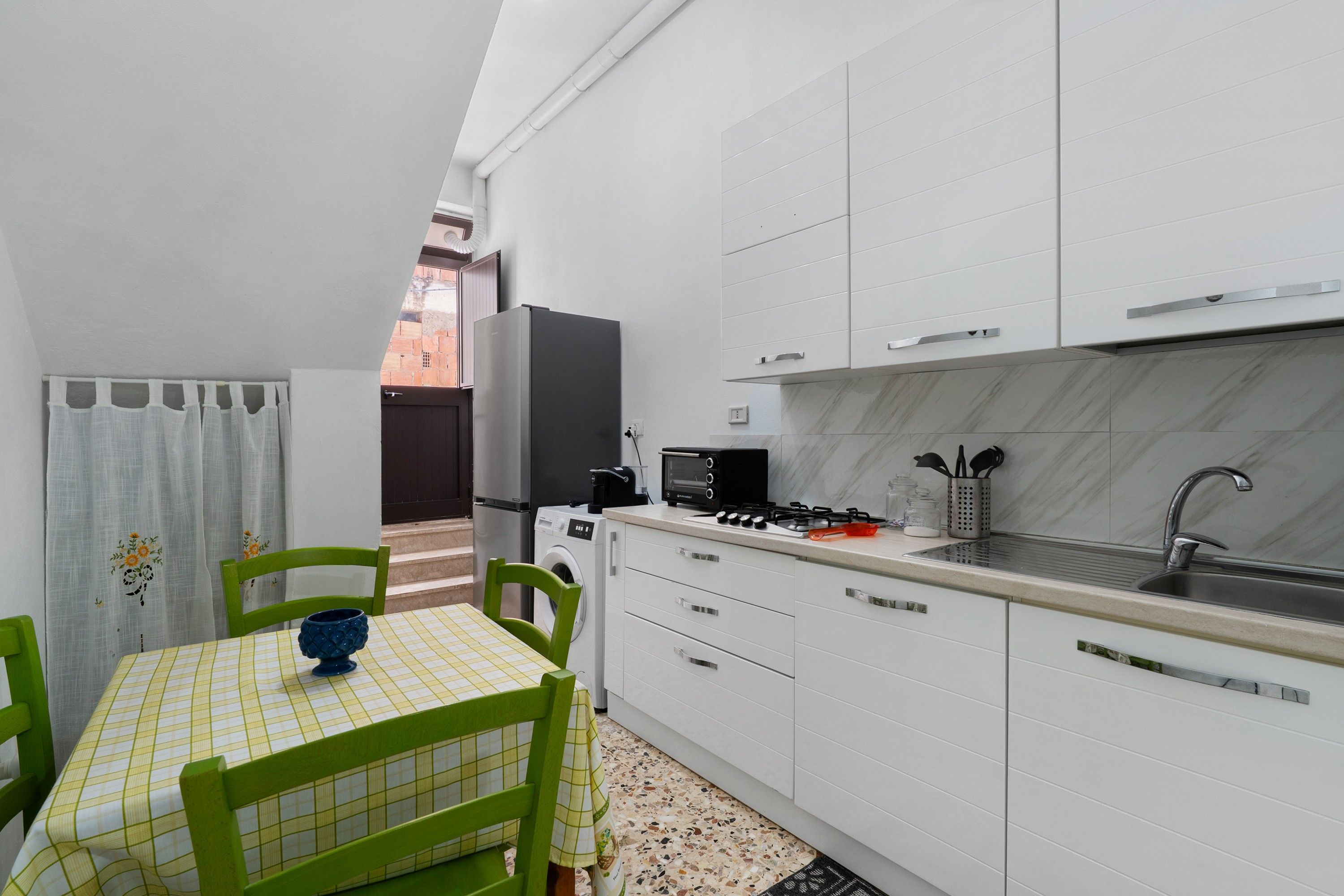 A compact kitchen with white cabinets, a sink, a stove, and a washing machine.