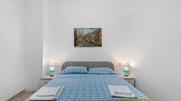 Ein Schlafzimmer mit einem Bett, zwei Nachttischlampen, einem Wandbild und einer gemusterten Bettdecke.