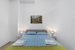 Ein Schlafzimmer mit einem Bett, zwei Nachttischlampen, einem Wandbild und einer gemusterten Bettdecke.
