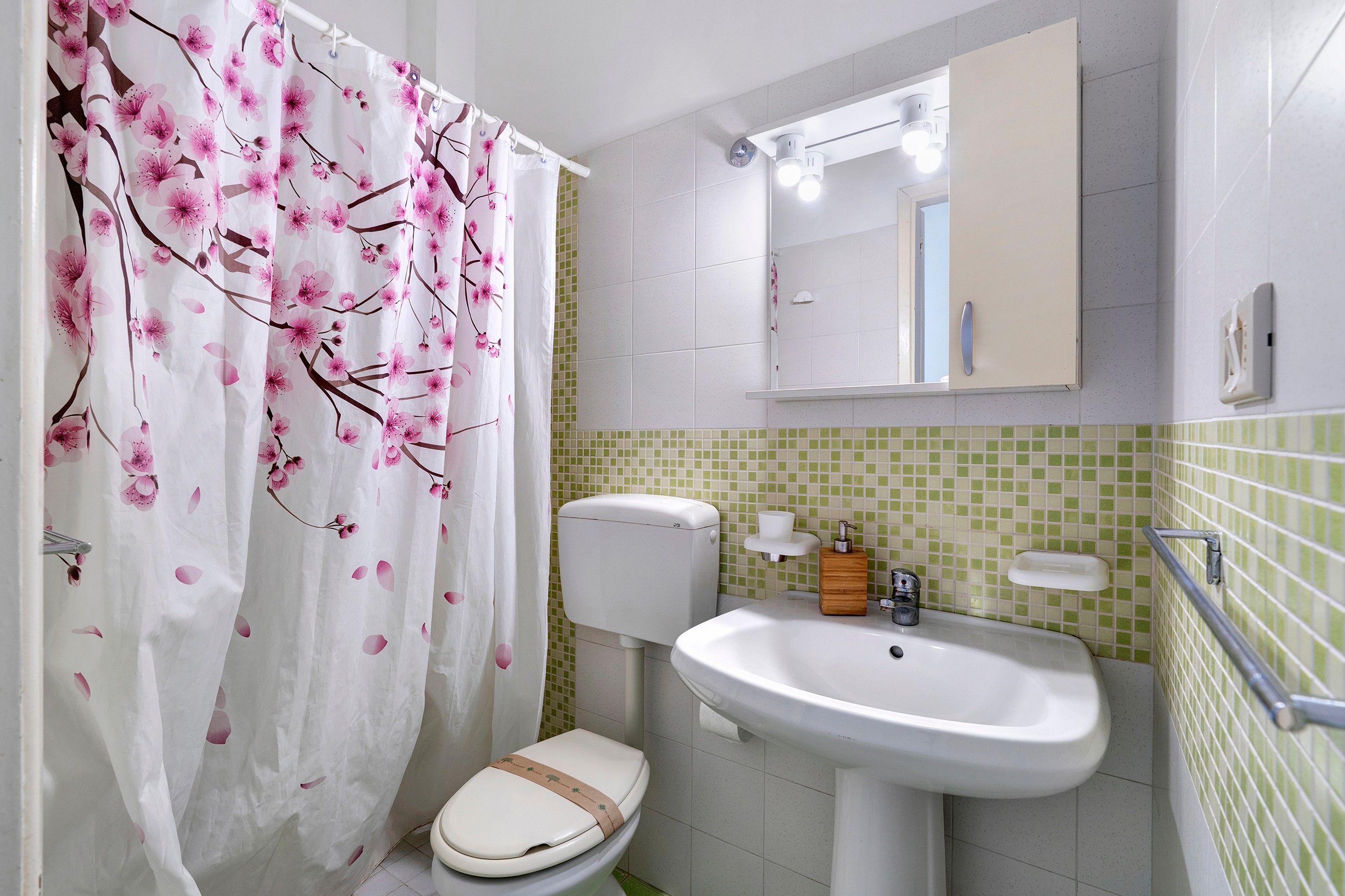 Une salle de bain équipée de toilettes, d’un lavabo et d’un rideau de douche à motifs floraux.