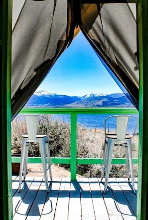 Blick durch ein Fenster auf eine Berglandschaft und ein Gewässer, zwei Stühle sind darauf ausgerichtet.