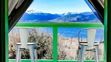 A view through a window with two chairs facing a mountainous landscape and a body of water.