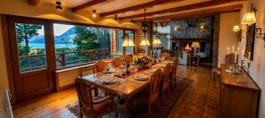 Een eetkamer met een lange tafel gedekt voor zes personen, een open haard en uitzicht op een bergachtig landschap door grote ramen.
