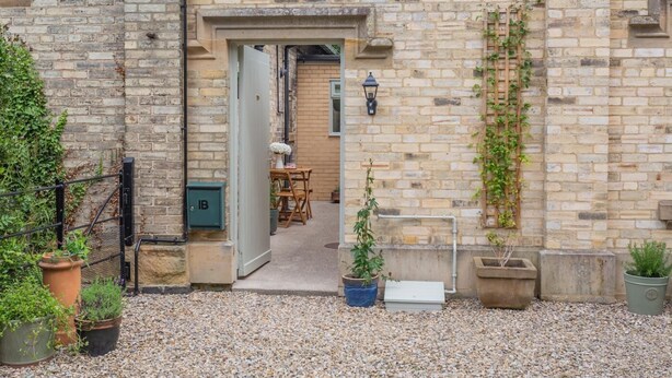 A stone building with a door leading to a room with a table and chairs, a potted plant, and a wall-mounted light fixture. - 1 Bed in Great Ayton (oc-h44914) (Great Ayton)