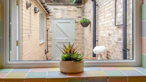 A window view of a brick building with a door, a potted plant on the windowsill, and a hanging plant. - 1 Bed in Great Ayton (oc-h44914) (Great Ayton)