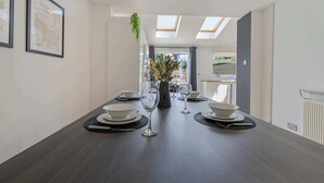 Un comedor con una larga mesa dispuesta para cuatro personas, obras de arte enmarcadas en las paredes y un tragaluz arriba.