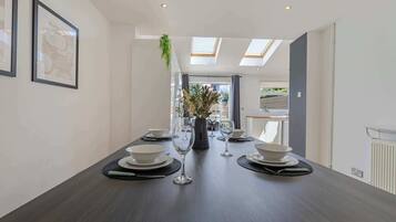 A dining room with a long table set for four, framed artwork on the walls, and a skylight above.
