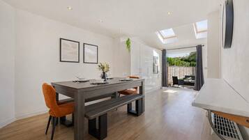 A modern dining area with a wooden table, chairs, and a bench. There are ceiling lights and a skylight.
